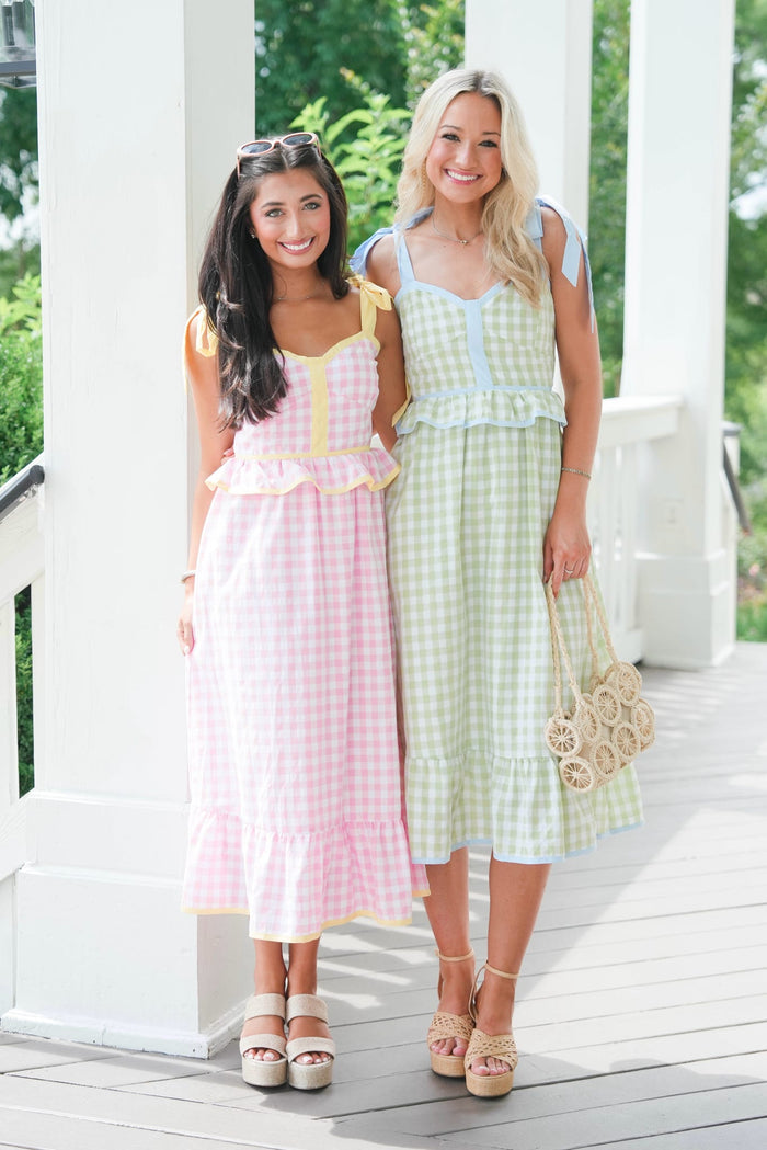 Two women in pastel checkered dresses standing on a wooden deck.