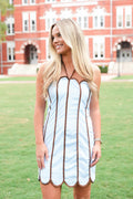 A woman wearing a light blue halter dress with brown trim stands on a green lawn in front of a red brick building.