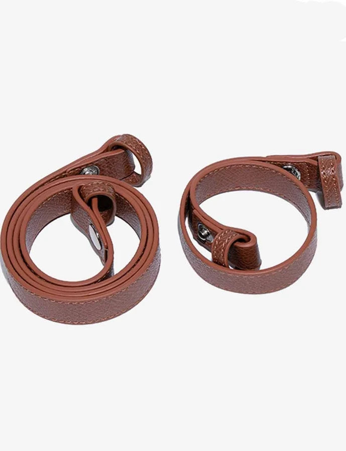 A pair of brown leather straps, likely camera straps or belt-like accessories, coiled and laid flat on a light gray background.