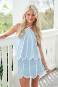 Woman wearing a light blue dress with white trim on a white railing.