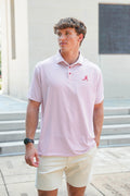 A man wearing a light pink and white horizontally striped polo shirt with a red Alabama 'A' logo on the chest, paired with beige shorts, standing outdoors in front of a building.