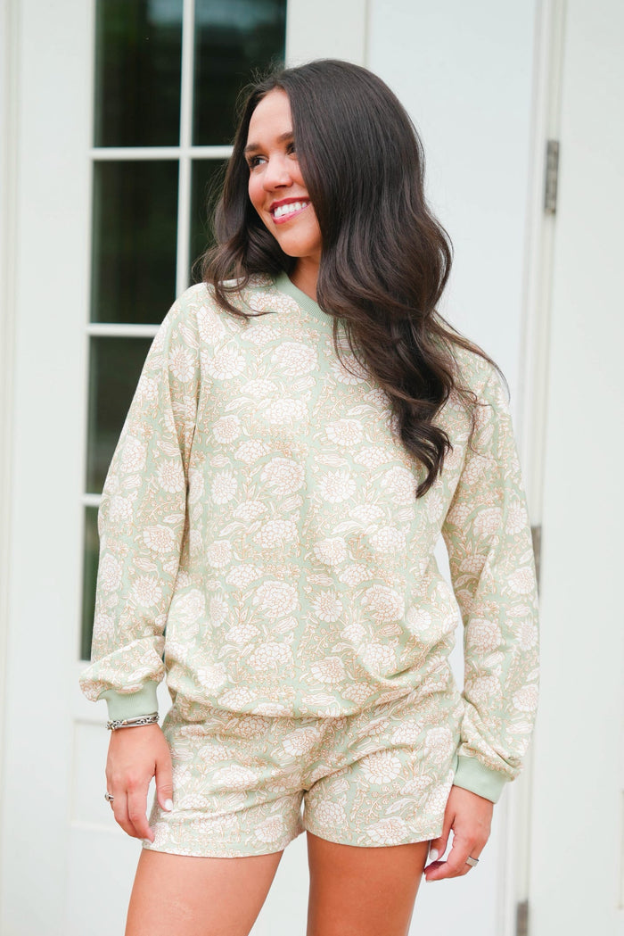 Woman wearing a light green floral pajama set standing in front of a white door.