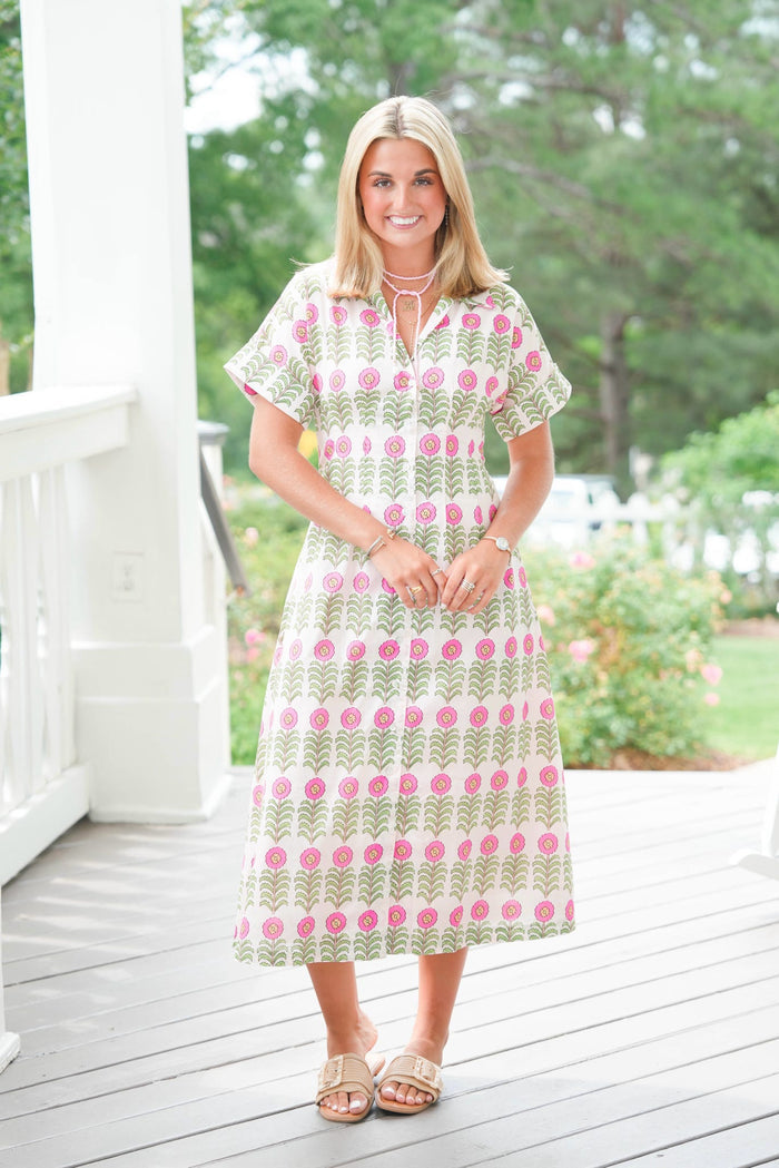 Woman wearing a patterned dress standing on a wooden deck with greenery in the background