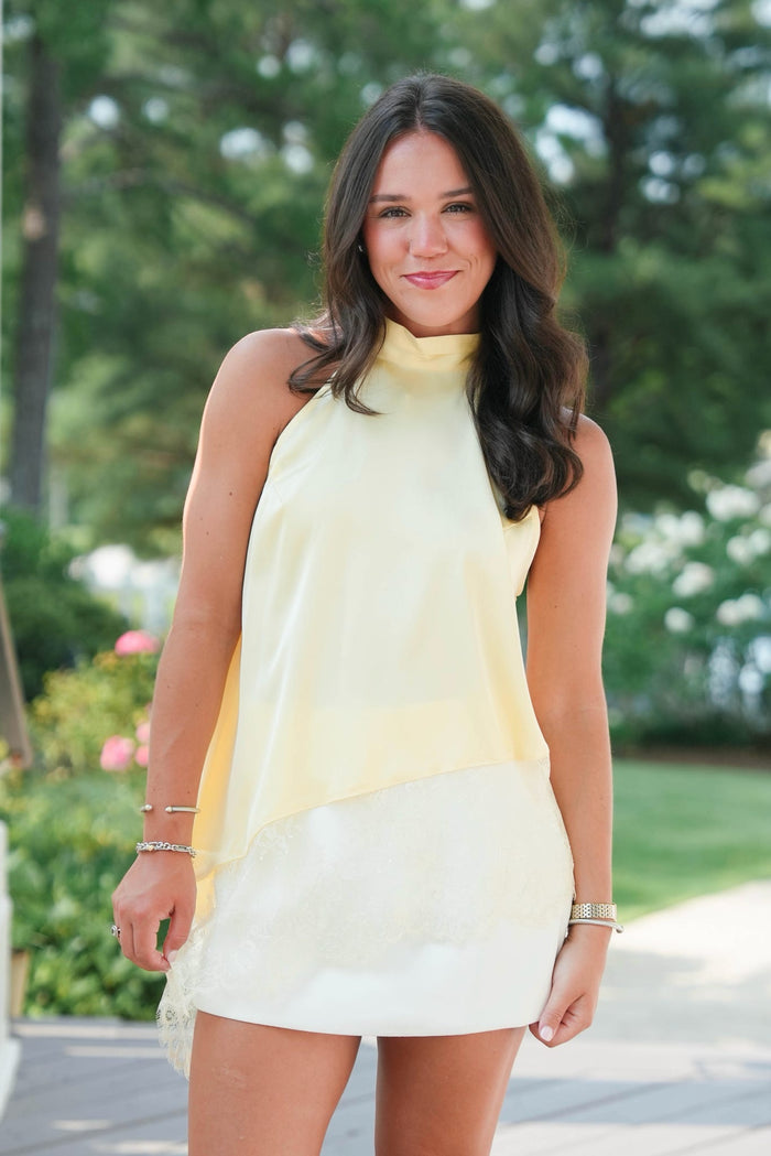 Woman wearing a yellow dress standing outdoors with greenery in the background