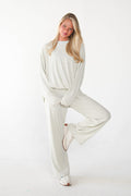 A woman modeling a matching cream-colored lounge set consisting of a long-sleeve top and wide-leg pants, posed against a seamless white studio background.