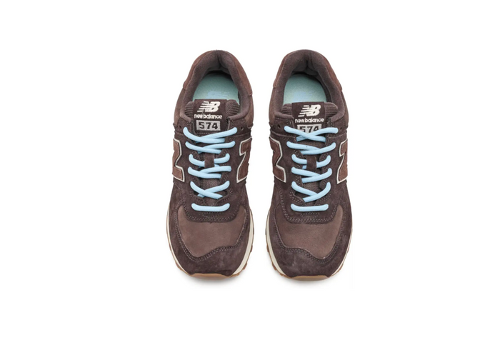 A pair of New Balance 574 sneakers in dark brown suede and mesh, featuring light blue laces and white side stripes, shown from a top-down view on a white background.