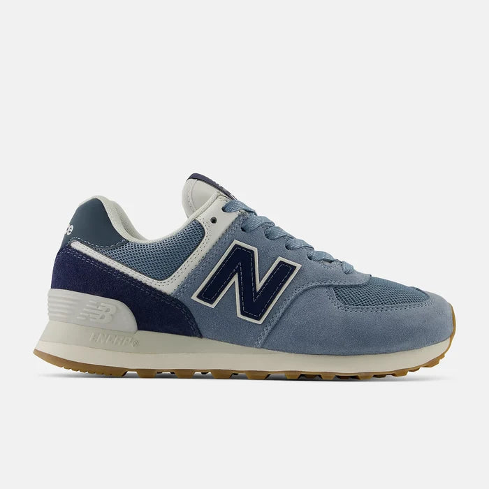 A New Balance sneaker in a mix of light blue suede, navy mesh, and white accents, with a brown gum sole, shown from the side on a light gray background.