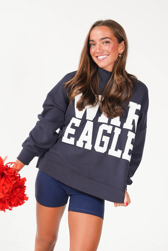 A woman modeling an oversized navy blue sweatshirt with bold white 'WHALE EAGLE' text across the front, paired with navy shorts, against a clean white background.