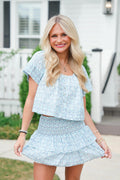 Woman wearing a light blue patterned outfit standing outdoors.