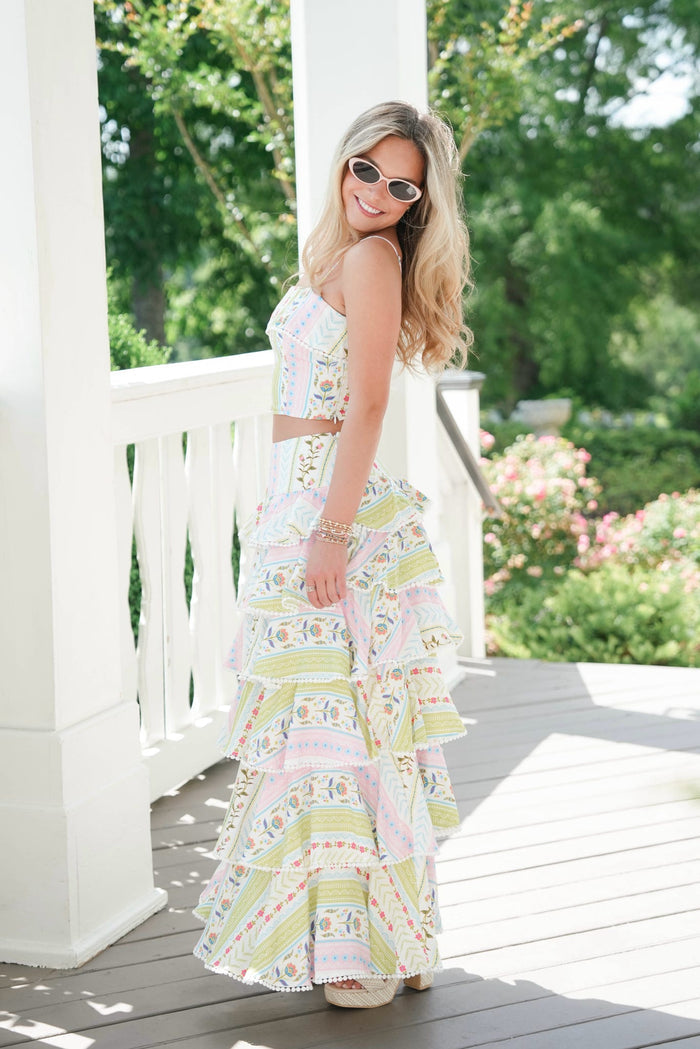 Woman in a floral dress standing on a porch with greenery in the background