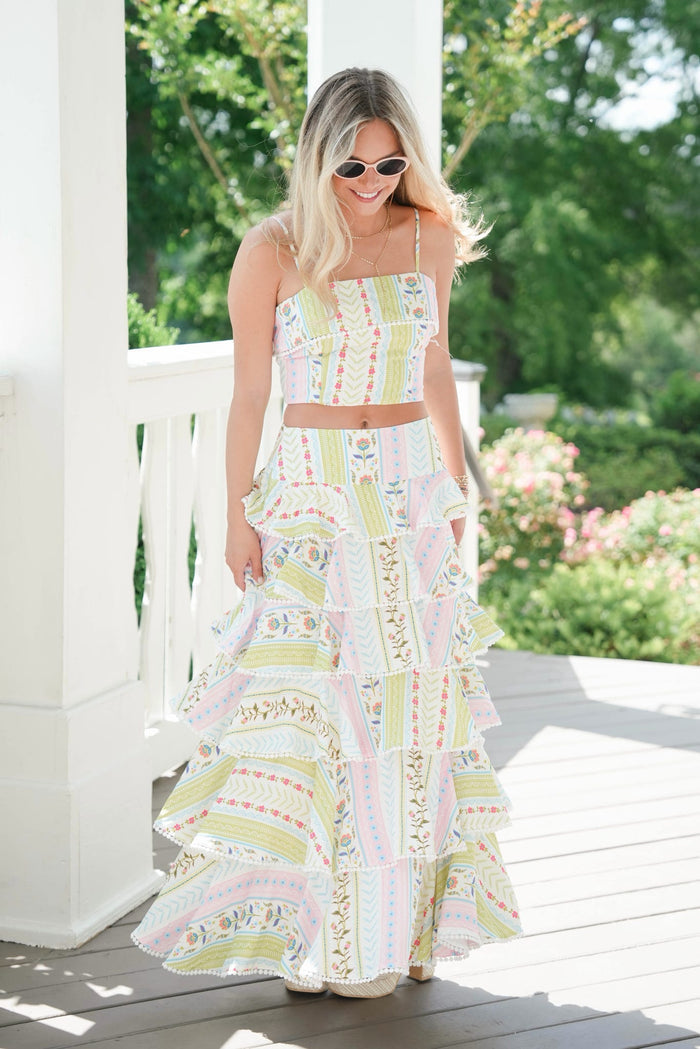 Woman in a colorful dress standing on a porch with greenery in the background