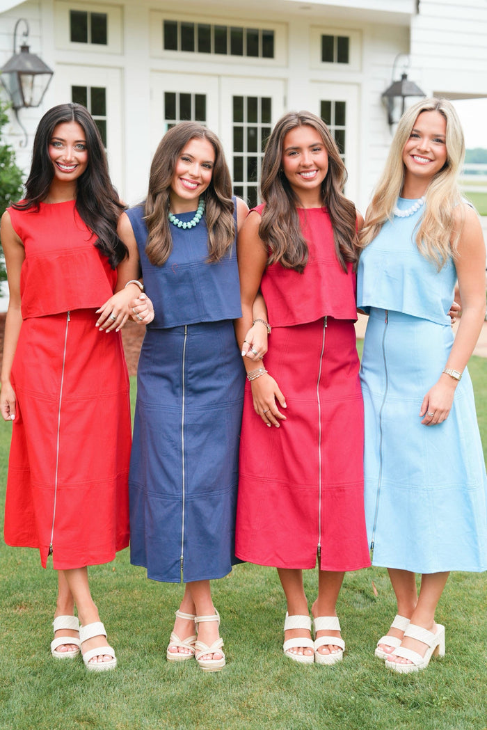 Four women in colorful dresses standing on grass with a building in the background
