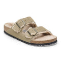 A pair of Birkenstock Arizona slide sandals featuring a sage green suede upper, plush cream shearling lining, cork footbed, and adjustable double straps with silver buckles.