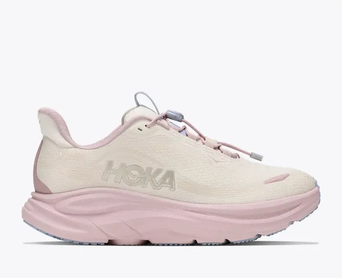 A Hoka trail running shoe in light cream and pastel pink, shown from a side profile view against a clean white background.