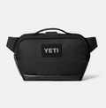 A black YETI shoulder bag with a top handle and a black rectangular patch on the front featuring the white YETI logo, set against a light gray background.