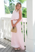 Woman in a pink dress standing on a wooden deck with greenery in the background