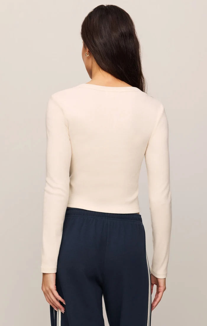 Woman wearing a beige long-sleeve top and navy pants on a plain background