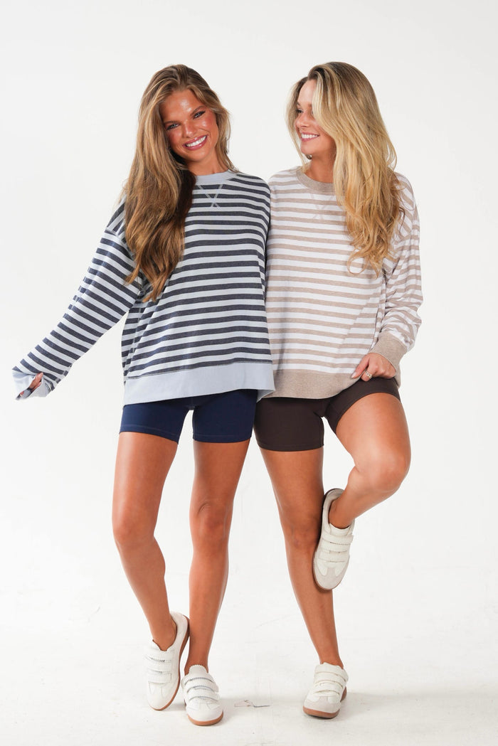 Two women modeling striped crewneck sweatshirts and biker shorts against a plain white studio background. One sweatshirt is navy and white striped, paired with navy shorts.