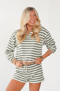 A blonde woman modeling a matching two-piece loungewear set consisting of a long-sleeve knit top and shorts, both featuring horizontal sage green and white stripes with a beige drawstring waist.
